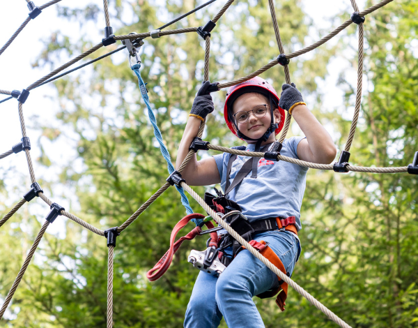 Ein Kind mit Kletterausr�stung klettert in einem Kletternetz und schaut in die Kamera